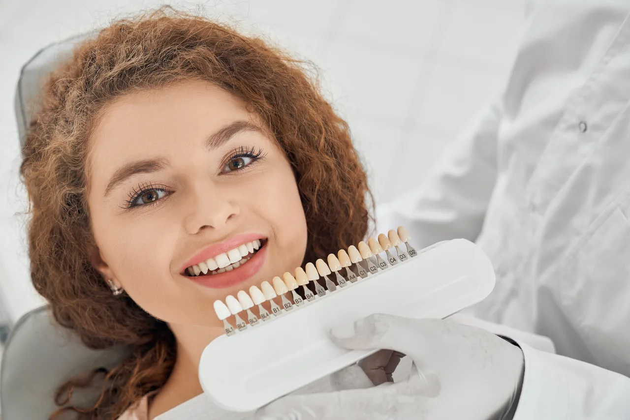Patient smiling while a dentist compares porcelain veneer shades